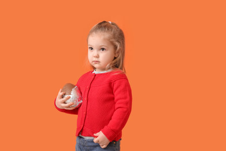 Cute little girl with chocolate Easter egg on color background