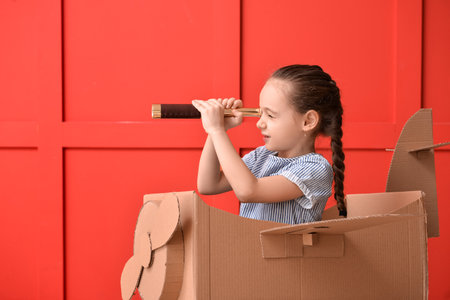 Little girl playing with spyglass and cardboard airplane near color wallの写真素材