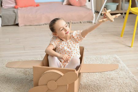 Little girl playing with toy and cardboard airplane at homeの写真素材