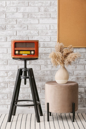 Retro radio receiver on table and pouf with vase near brick wallの写真素材