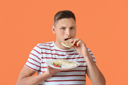 Young man eating tasty quesadilla on color backgroundの写真素材