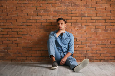 Depressed young man sitting near brick wallの写真素材
