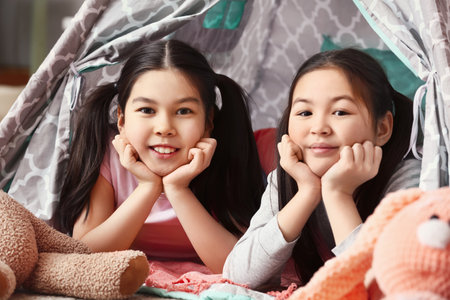 Cute Asian sisters lying in play tent at homeの写真素材