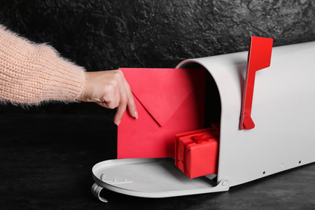 Woman taking letter from mailbox on dark background. Valentine's Day celebration