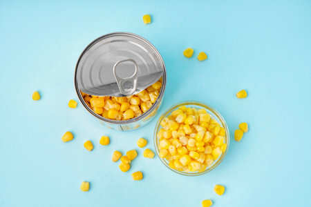 Tin can and bowl with corn kernels on blue backgroundの写真素材