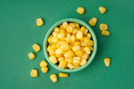 Bowl with canned corn kernels on green background