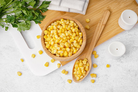 Cutting board with spoon and bowl of canned corn kernels on white table