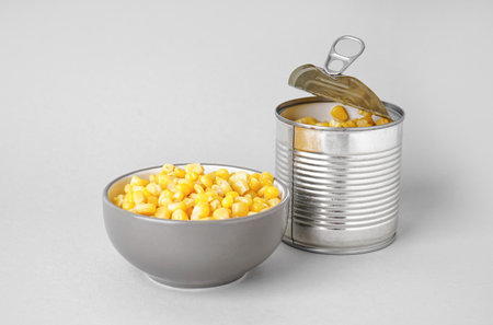 Bowl and tin can with canned corn on gray background