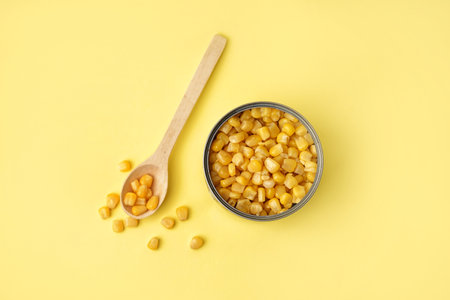 Tin can and spoon with corn kernels on yellow background