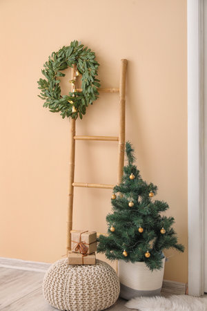 Ladder with Christmas wreath, fir tree and pouf near beige wall in roomの写真素材