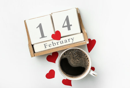 Cube calendar with date 14 FEBRUARY, cup of coffee and hearts on white background