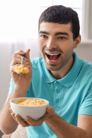 Happy young man eating cornflakes with spoon at home, closeup
