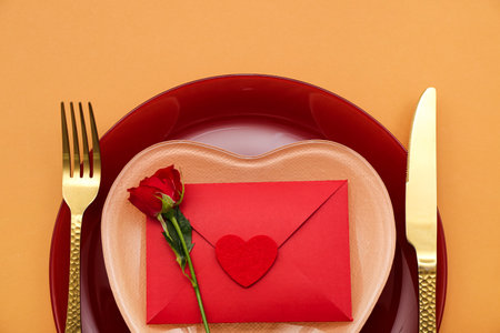 Table setting for Valentine's Day with envelope and rose on orange background, closeupの写真素材