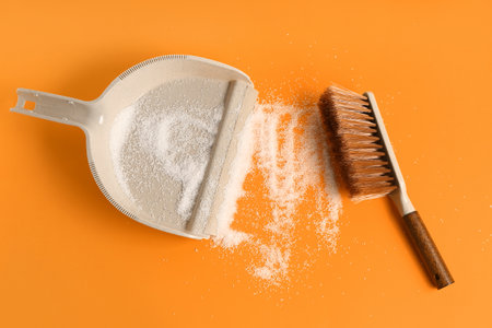Dustpan with sugar and brush on orange background