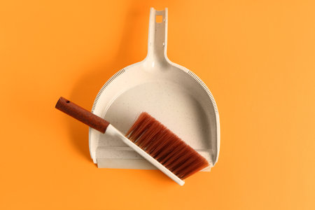 Dustpan and brush on orange background