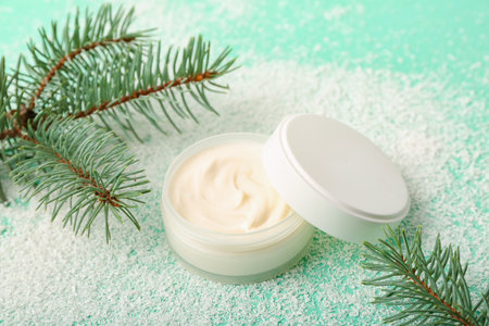 Jar of cream, fir branches and snow on color backgroundの写真素材