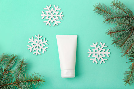 Composition with tube of cream, fir branches and snowflakes on color backgroundの写真素材