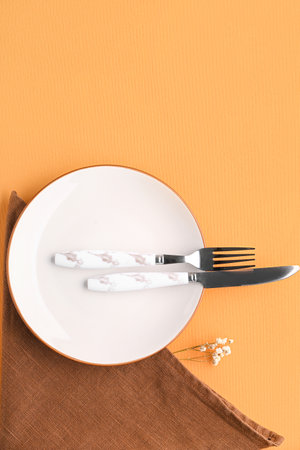 Plate with cutlery, floral decor and napkin on orange backgroundの写真素材
