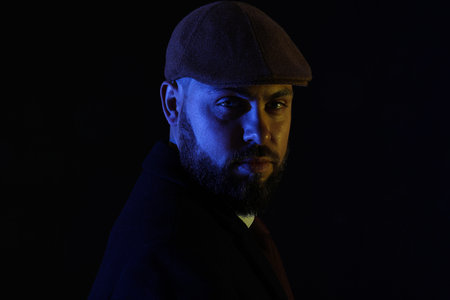 Silhouette of young bearded man in cap on dark background, closeup