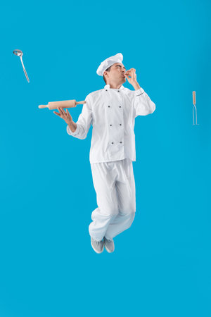 Young chef with cooking supplies jumping on blue backgroundの写真素材