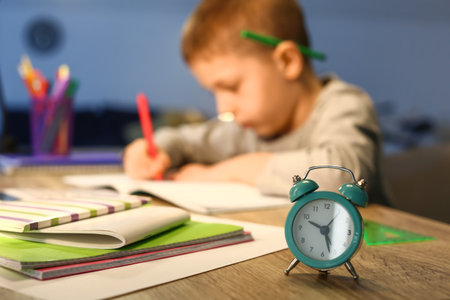 Alarm clock on table of little boy doing homework at home late in the evening