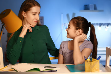 Little girl with her mother doing homework at home late in the evening