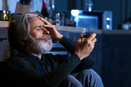 Drunk senior man with glass of drink in kitchen at nightの写真素材