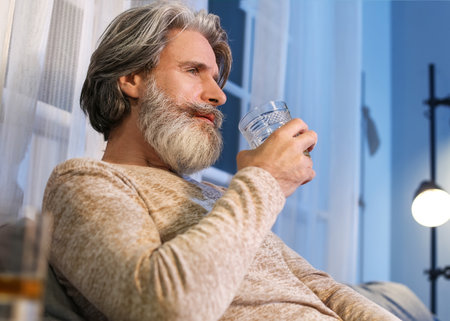Senior man drinking alcohol from glass late in the evening at homeの写真素材