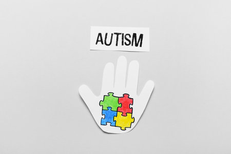 Paper human palm with colorful puzzle pieces and word AUTISM on light background