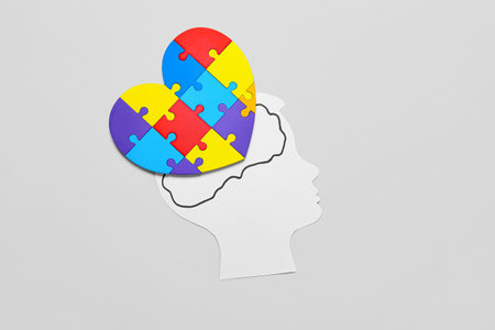 Paper human head with colorful puzzle pieces in shape of heart on light background. Concept of...