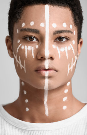Young African-American guy with paint on face against light backgroundの写真素材