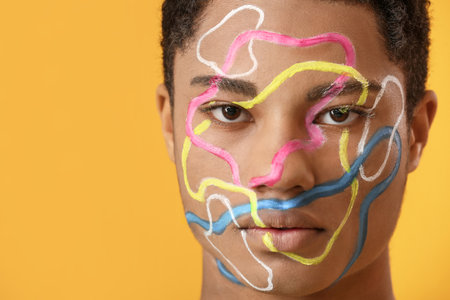 Young African-American guy with paint on face against color background, closeup