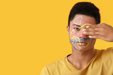 Young African-American guy with paint on face against color background