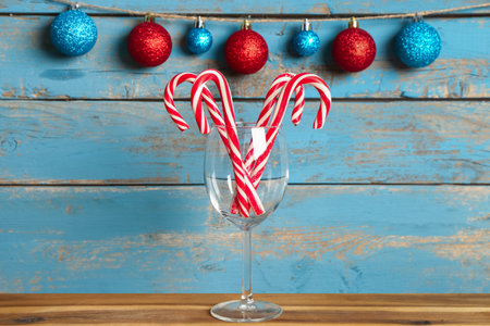 Wine glass with tasty candy canes and Christmas balls on table against color wooden backgroundの写真素材