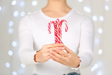 Woman holding tasty candy canes against blurred Christmas lightsの写真素材