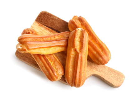Wooden cutting board with delicious eclairs on white backgroundの写真素材