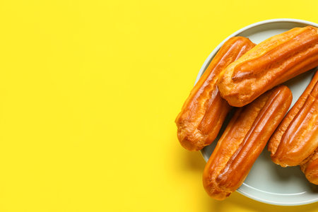 Plate with tasty eclairs on yellow backgroundの写真素材