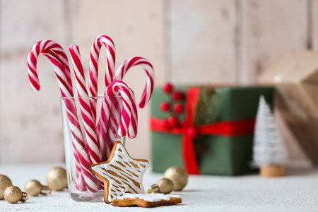 Glass with tasty candy canes, cookies and Christmas balls on table
