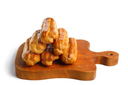 Wooden cutting board with tasty eclairs isolated on white background