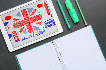 Tablet computer and stationery on dark background. Concept of learning English