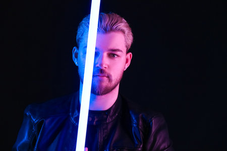 Toned portrait of handsome young man with neon lamp on dark backgroundの写真素材