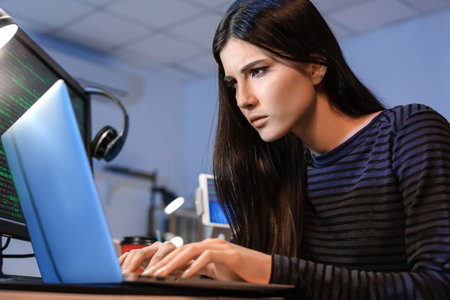 Female programmer working with laptop in office at nightの写真素材