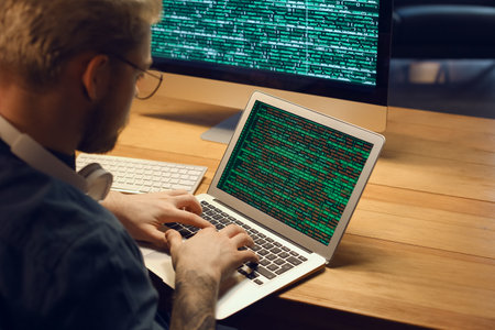 Young programmer working with laptop in office at night