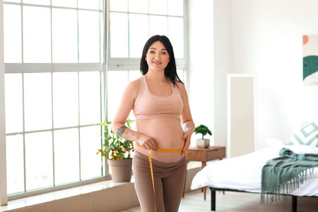Young pregnant woman measuring her belly at homeの写真素材