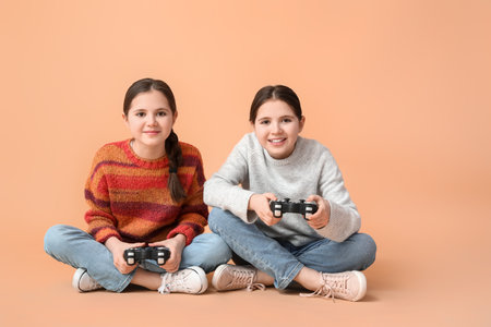 Cute twin girls playing video game on color background