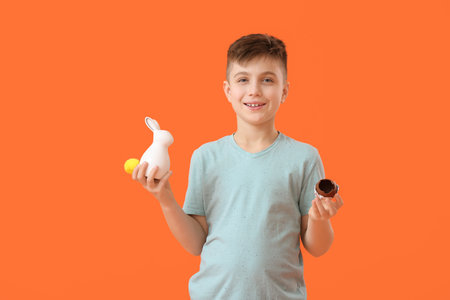 Cute little boy with chocolate Easter egg and figurine of bunny on color background