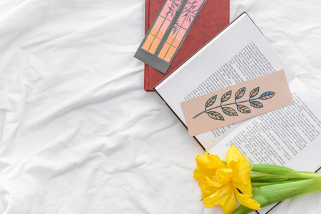Books with bookmarks and flower on bed