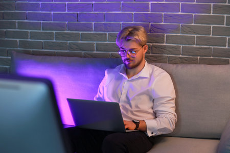 Handsome man using laptop in office at nightの写真素材