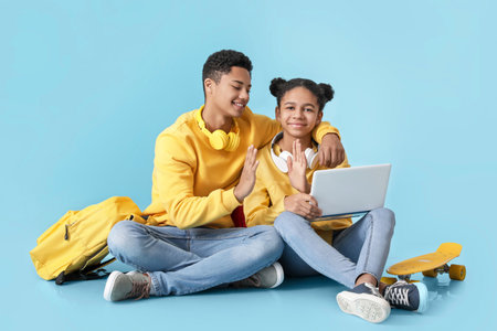 African-American brother and sister with laptop giving each other high-five on color background