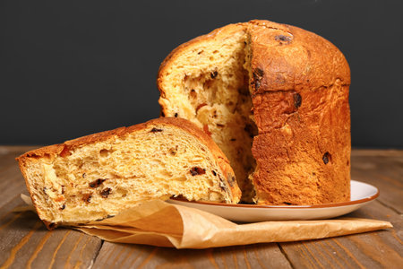 Plate with cut Panettone and baking paper on table against black background